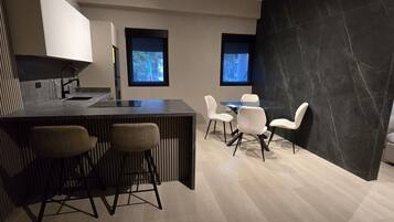 A modern kitchen with a bar area, two windows, and a dining area with white chairs.