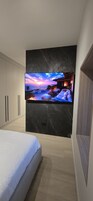 A bedroom with a large TV mounted on a marble wall, a bed, and a wooden cabinet.