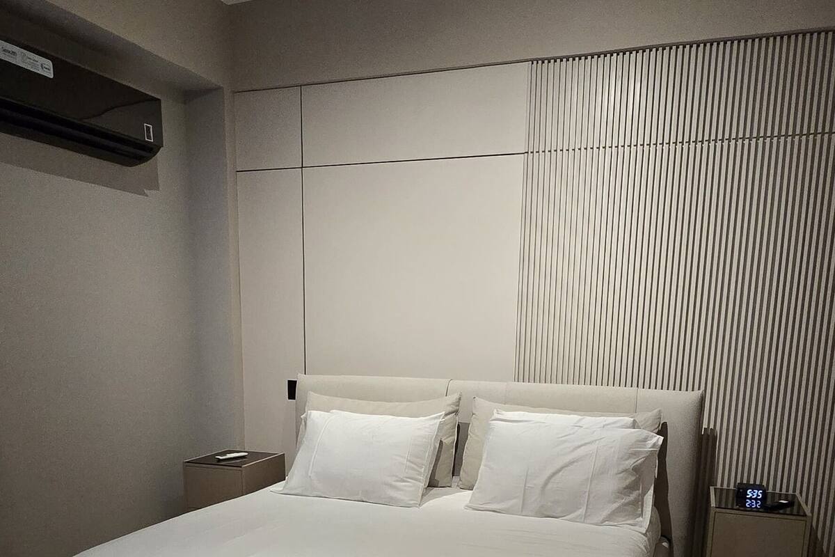 A modern bedroom with a large bed, a bedside table, a nightstand, and a wall-mounted air conditioner.