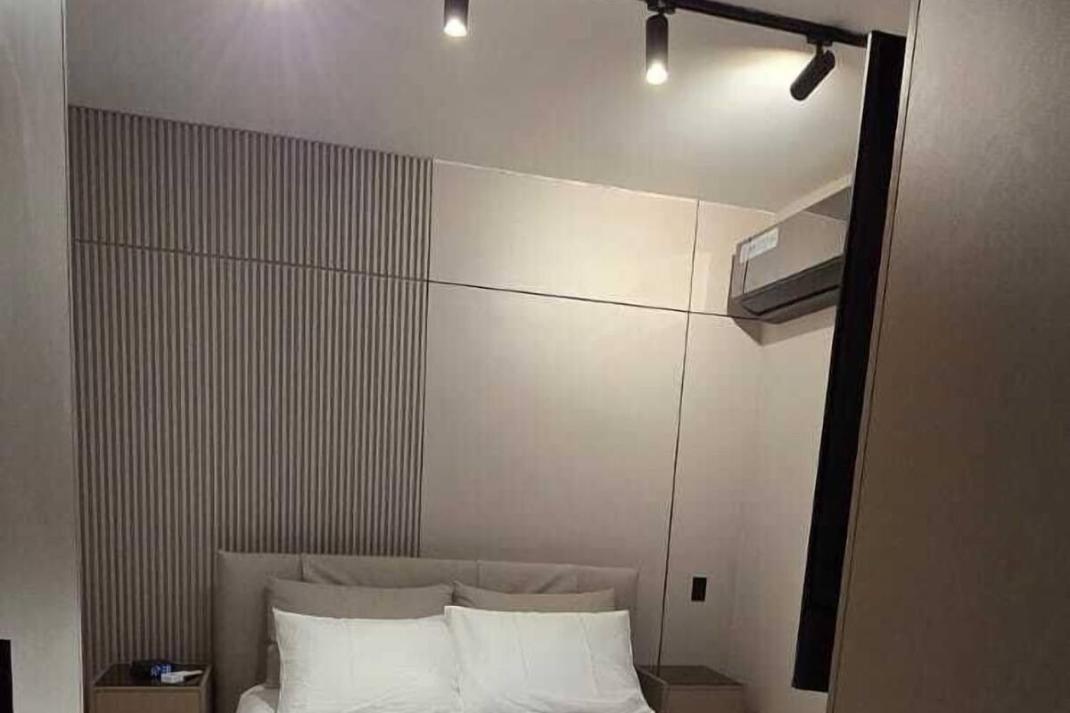 A modern bedroom with a bed, bedside tables, and a wall-mounted air conditioner.