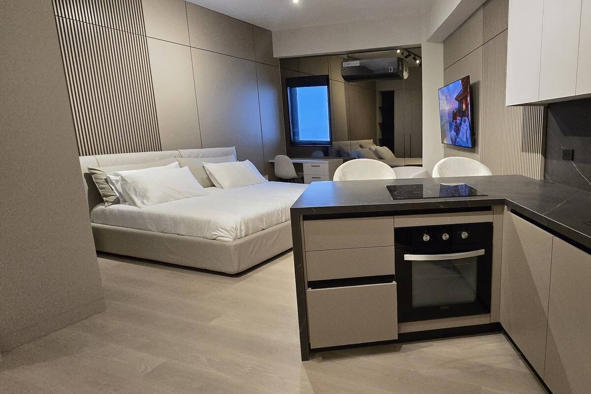 A compact hotel room with a kitchenette, a bed, a desk, and a TV.