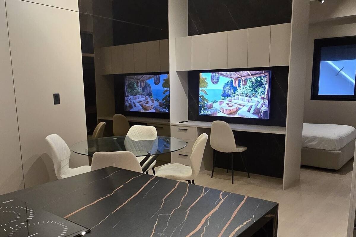 A modern living room with a marble dining table, two flat-screen TVs, and comfortable seating.