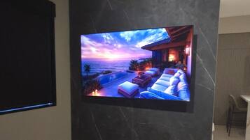 A modern bedroom with a large flat-screen TV mounted on a marble wall, a bed with white bedding, and a pair of slippers on the floor.