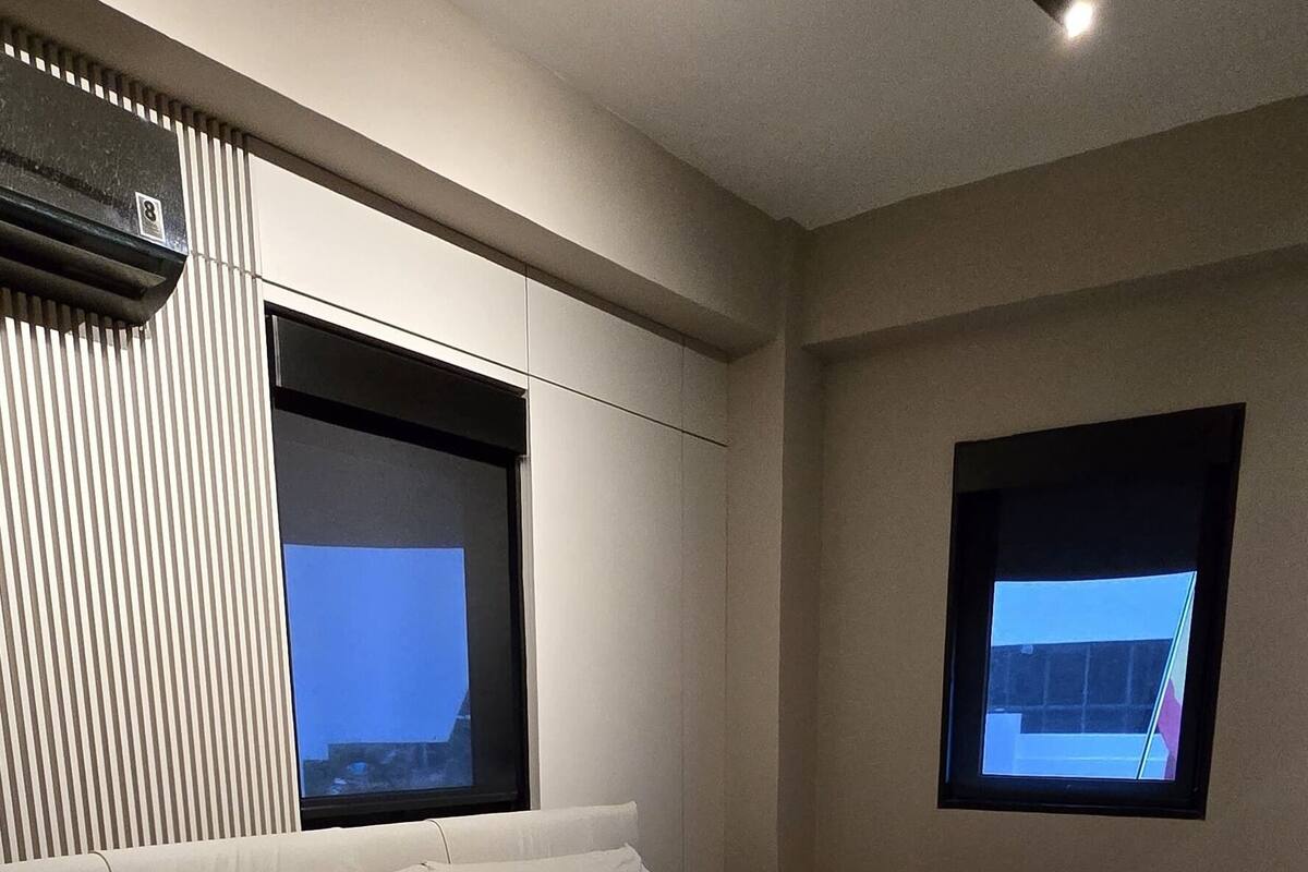 A modern bedroom with a large bed, two windows, and a ceiling light.