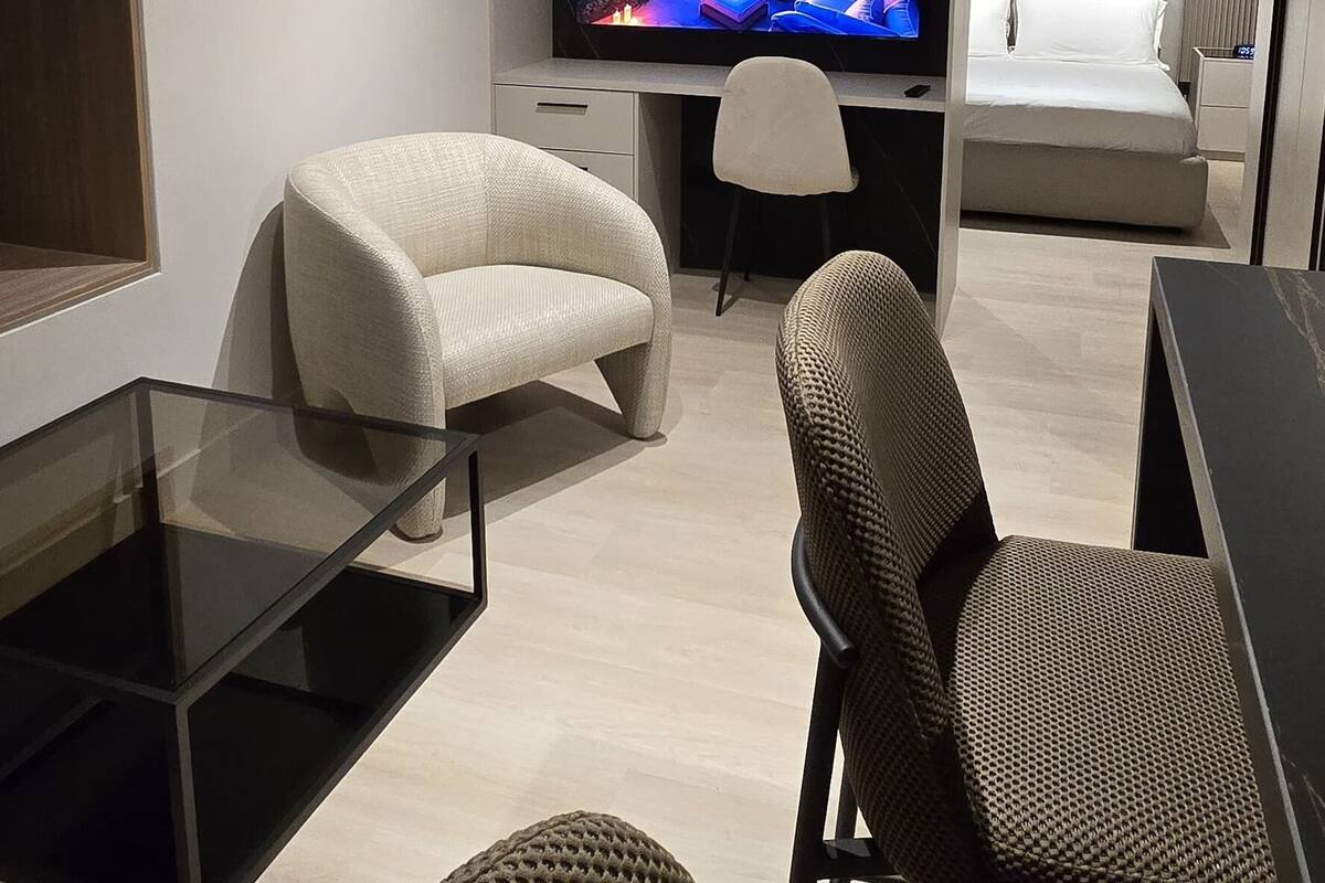 A modern living room with a flat-screen TV, a sofa, a chair, and a glass coffee table.