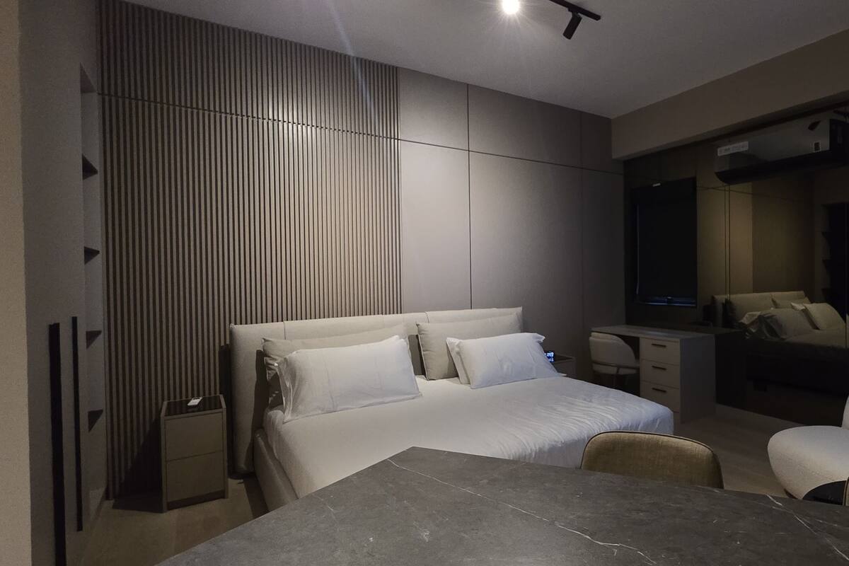 A modern hotel room with a large bed, a desk, a chair, a TV, and a dining table.