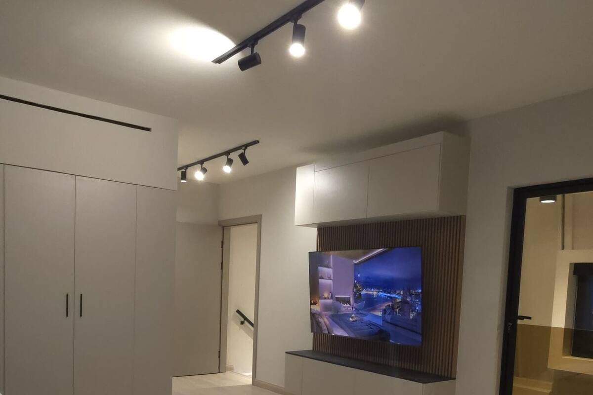 A modern bedroom with a large bed, a flat-screen TV mounted on the wall, and a wardrobe.