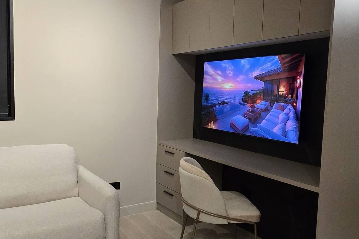 A modern living room with a flat-screen TV mounted on a wall, a white sofa, a chair, and a dark coffee table.