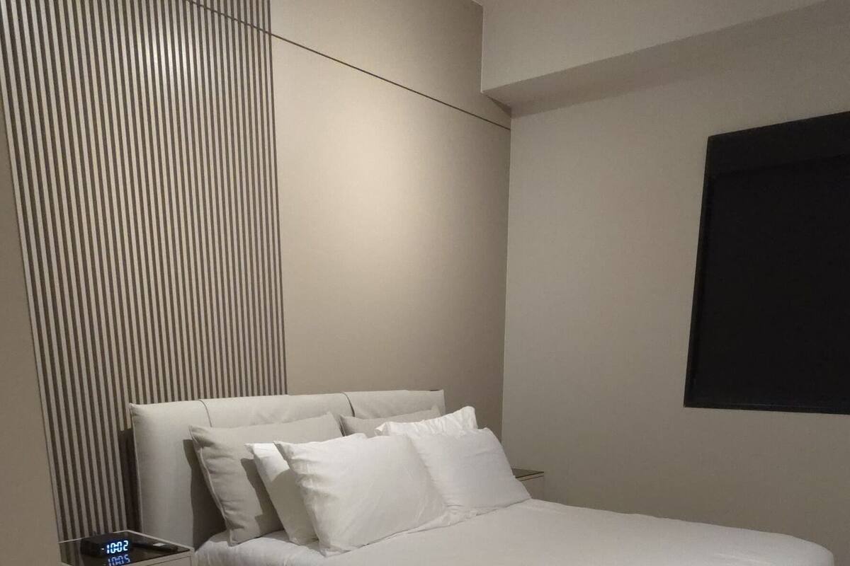 A modern bedroom with a large bed, a bedside table, and a wall-mounted light fixture.