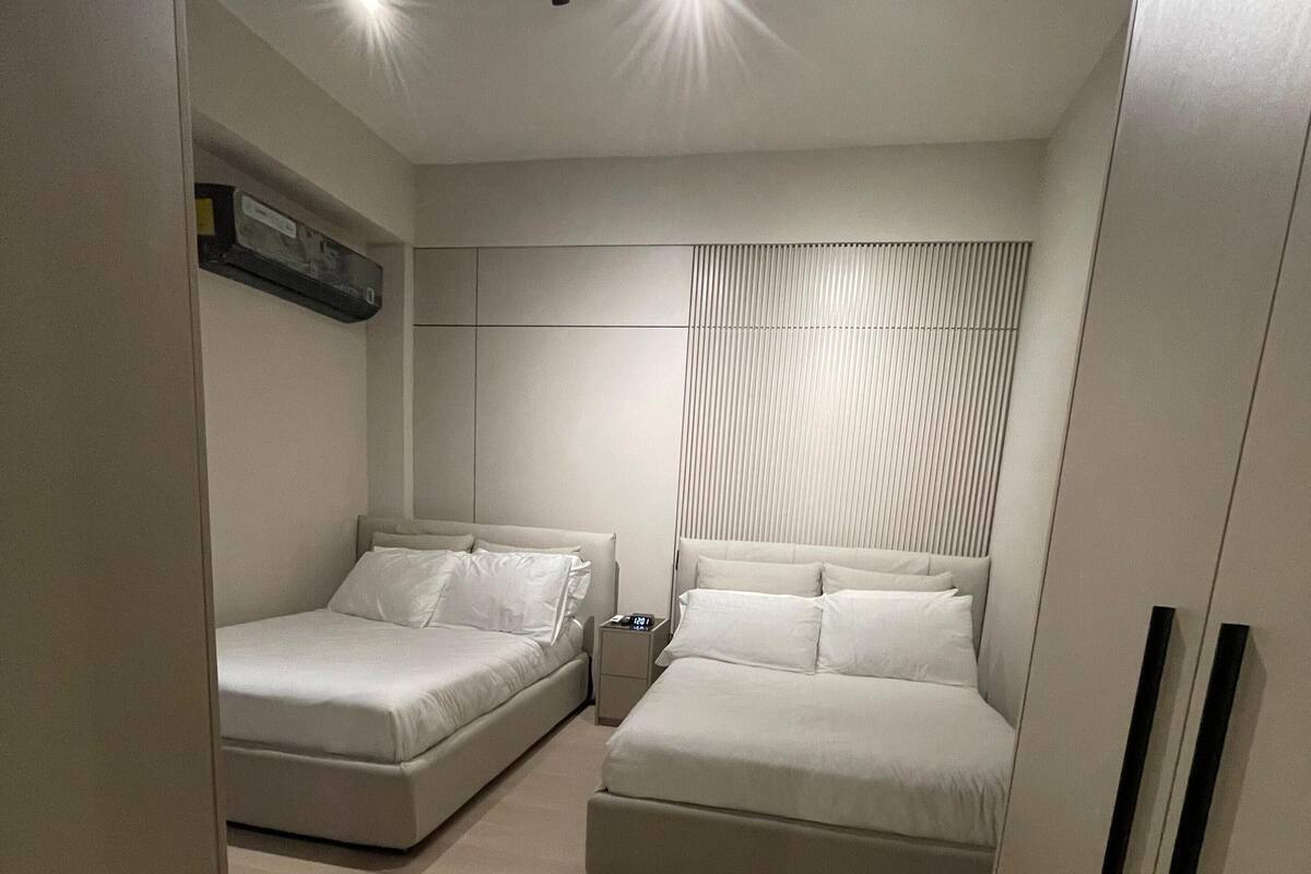 A modern bedroom with two beds, a nightstand, and a ceiling light fixture.