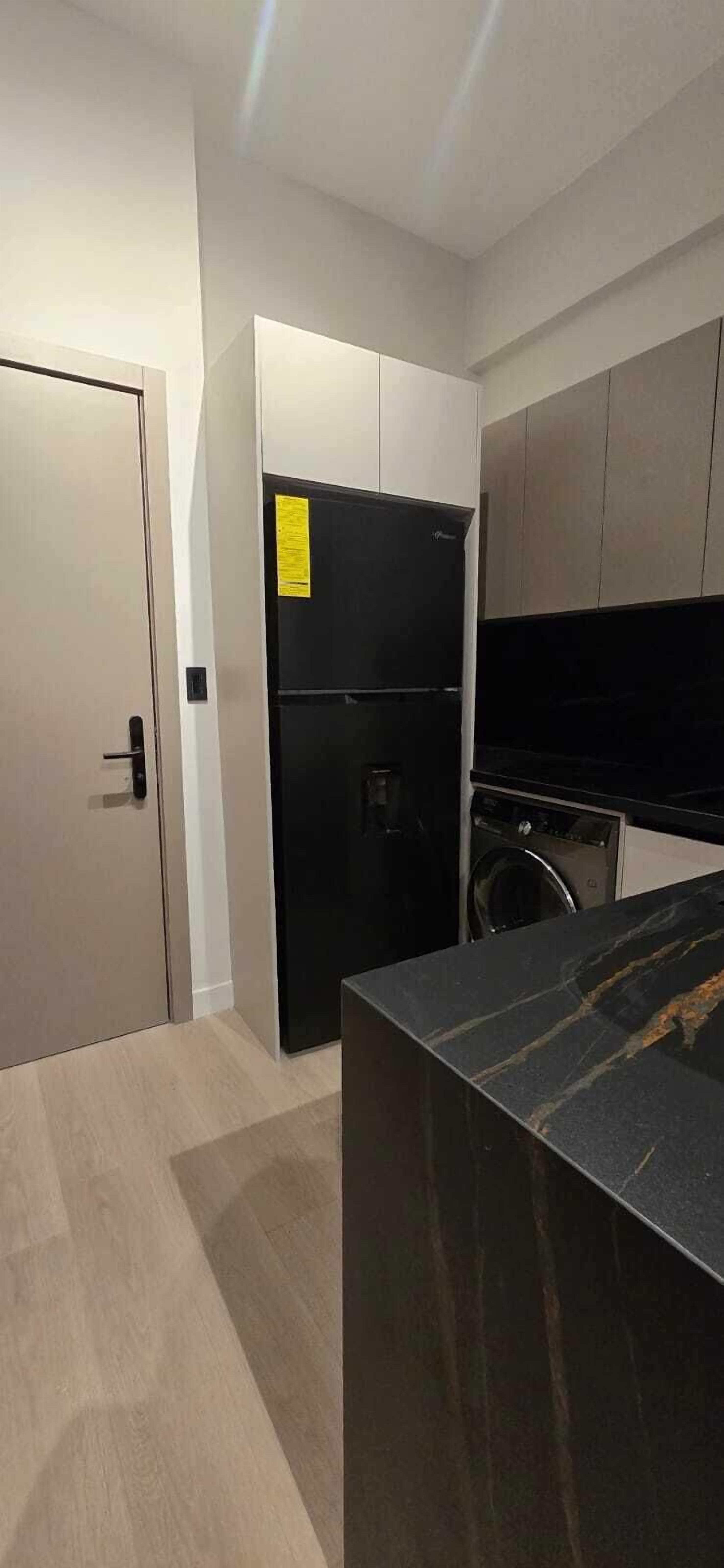 A modern kitchen with a black refrigerator, a washing machine, and a marble countertop.