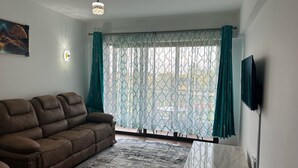 A living room with a brown sofa, a patterned rug, a white coffee table, and a TV mounted on the wall. - A vibrant and connected hub blending urban living, green spaces, and convenience (Nairobi)