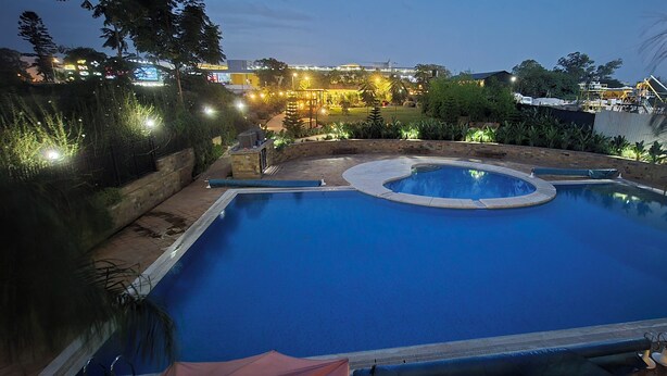 A swimming pool with a circular hot tub in the center, surrounded by a landscaped garden with various plants and a paved walkway. - A vibrant and connected hub blending urban living, green spaces, and convenience (Nairobi)