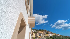 A coastal town with buildings on a hillside, a clear blue sky, and a white building in the foreground. - Velis - art & hospitality (Posada)