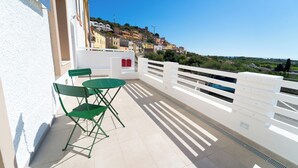 A balcony with a green table and chairs, overlooking a hillside of colorful buildings. - Velis - art & hospitality (Posada)