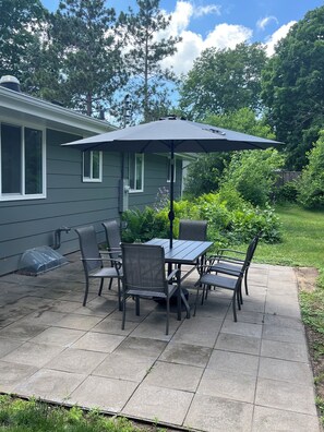A patio with a table and chairs, a covered umbrella, and a house in the background.