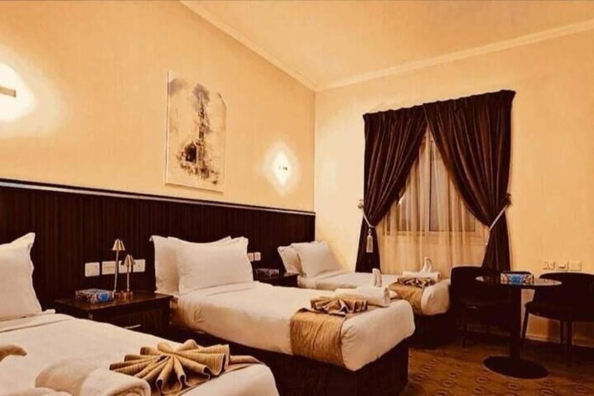 A hotel room with three beds, a desk, a flat-screen TV, and a window with curtains.