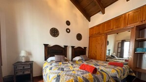 Un dormitorio con una cama grande, cabecera de madera, una mesita de noche con lámpara y un armario con espejo.