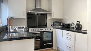 Una cocina moderna con armarios blancos, estufa de acero inoxidable, microondas y hervidor.