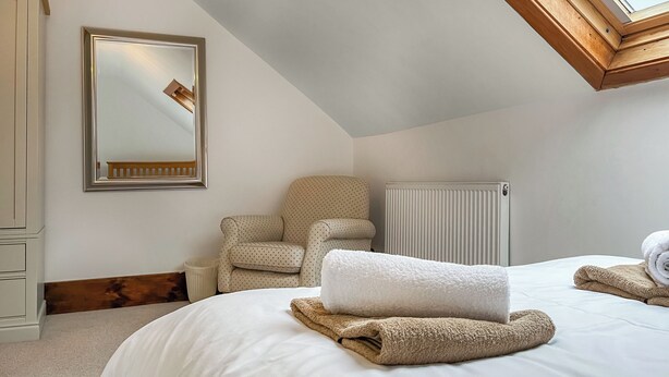 Un dormitorio con una cama grande, una silla, un radiador y un tragaluz.