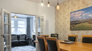 Un espacio abierto que combina sala y comedor, con una mesa de madera, sillas, un sofá y vistas al exterior a través de un ventanal.