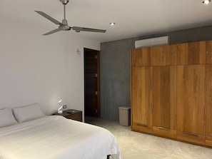 Een slaapkamer met een bed, nachtkastje, plafondventilator, kledingkast en een deur naar een andere kamer.