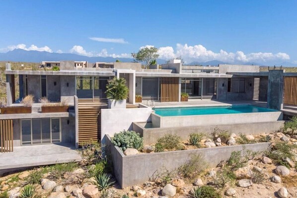 A modern residential complex with a central swimming pool, surrounded by landscaped gardens and a mountainous backdrop. - Arroyo Escondido -Luxe Oceanview Contemporary Home (Todos Santos)