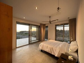 A bedroom with a large bed, a ceiling fan, and a view through the glass doors. - Arroyo Escondido -Luxe Oceanview Contemporary Home (Todos Santos)
