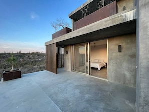 Un bâtiment moderne doté d’un toit plat, de grandes portes-fenêtres coulissantes donnant accès à une chambre, et d’une terrasse en béton.