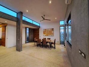 A spacious room with a dining table and chairs, a ceiling fan, and large windows.