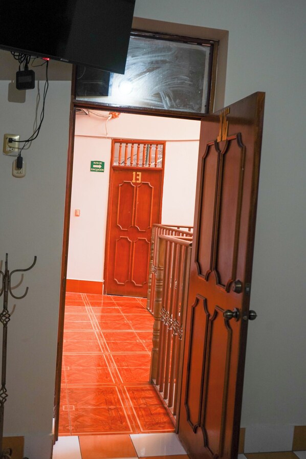 A hallway with a red door, a staircase, and a television mounted above.