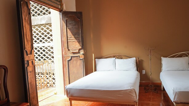 A bedroom with a wooden bed, a wooden chair, and a large wooden door with a lattice design. - Hotel El Conquistador (Veracruz)