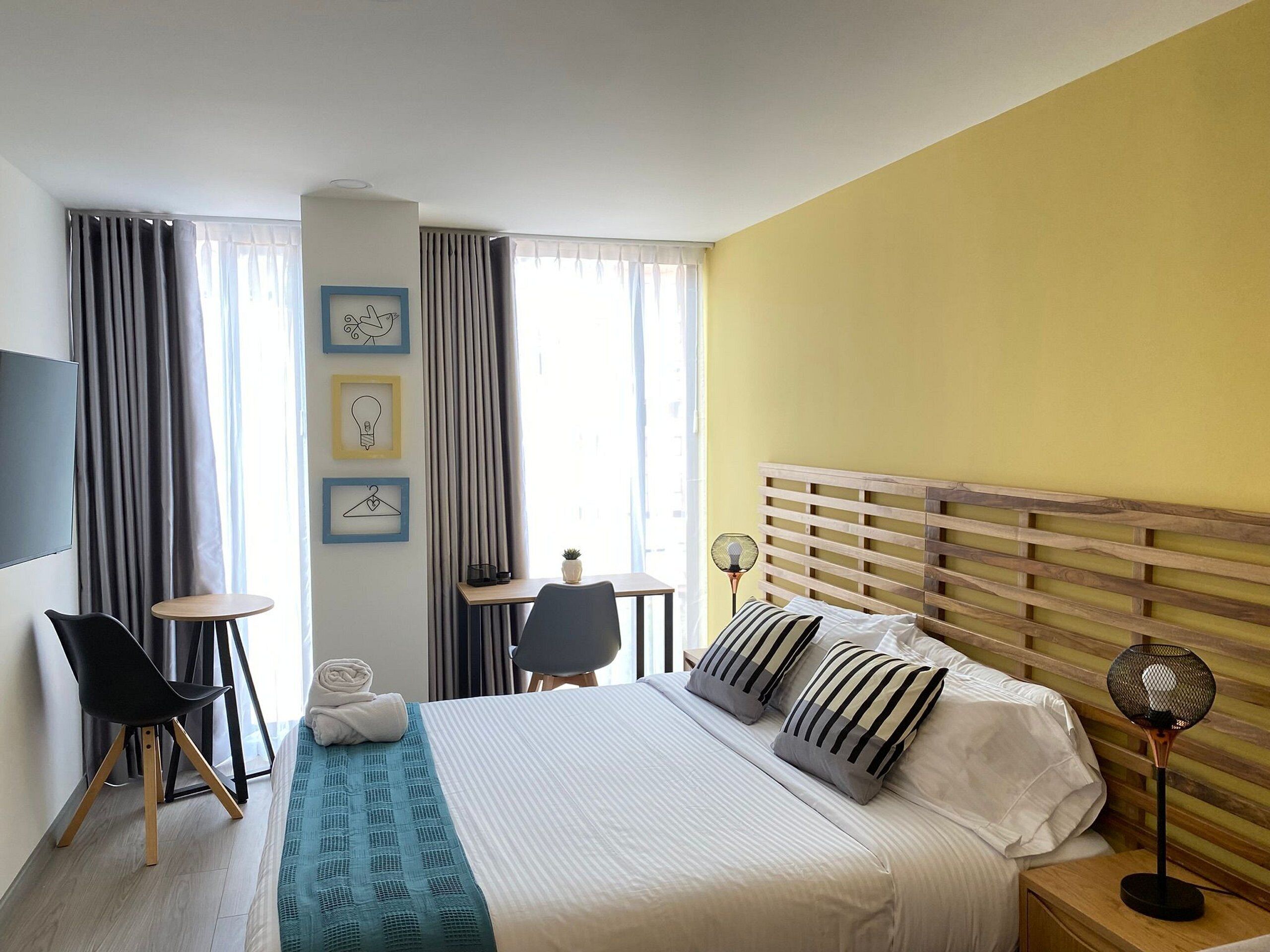 Une chambre d’hôtel avec un lit, un bureau, une chaise, une télévision et une fenêtre avec des rideaux.