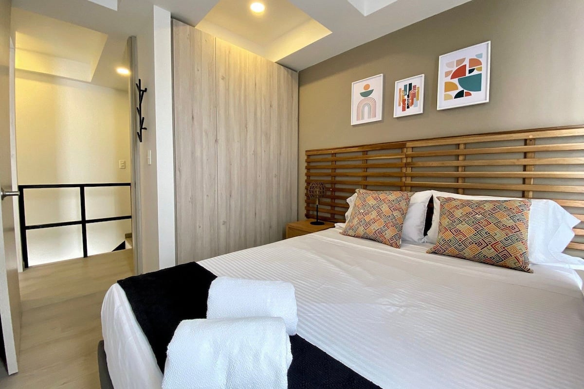 A modern hotel room with a large bed, wooden headboard, and three framed artworks on the wall.