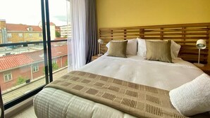 Una habitación de hotel con una cama grande, vistas de la ciudad a través de una ventana y un cabecero de madera.