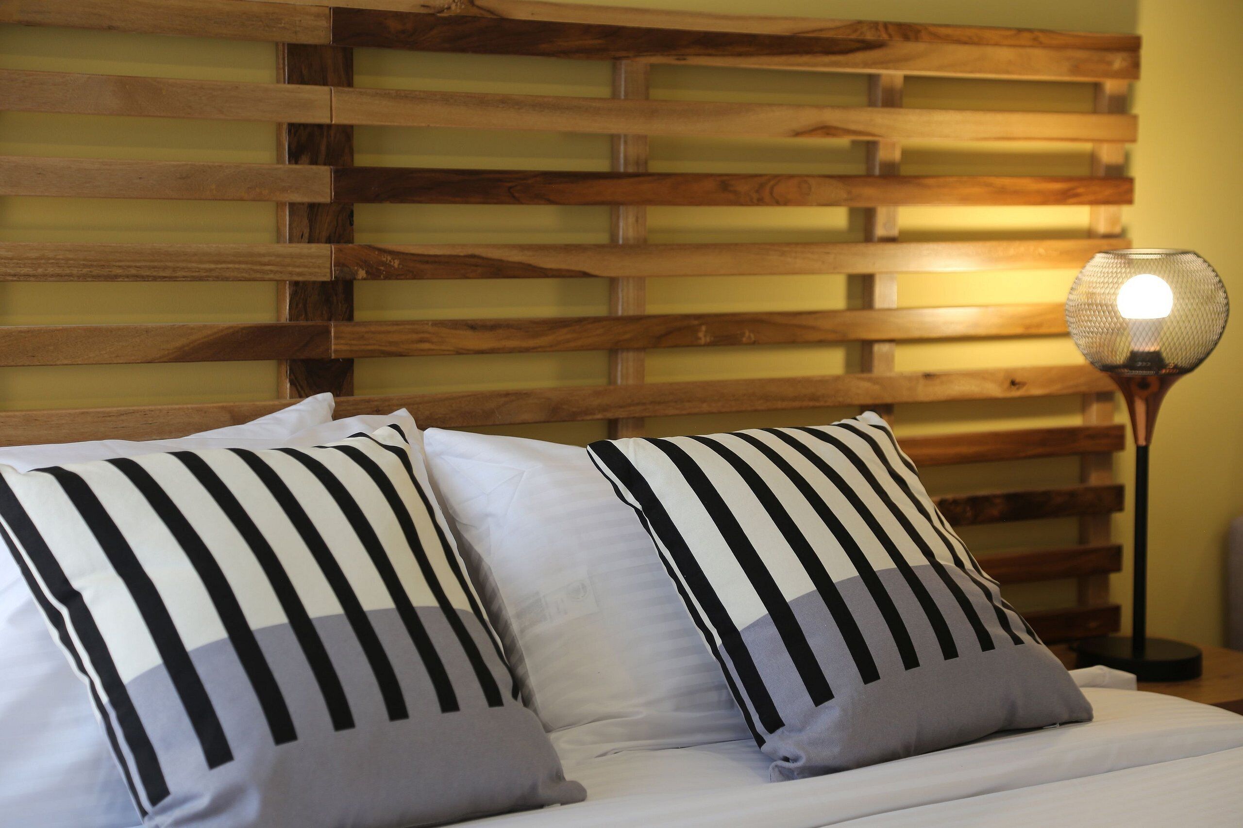 A bed with striped pillows, a wooden headboard, and a floor lamp.