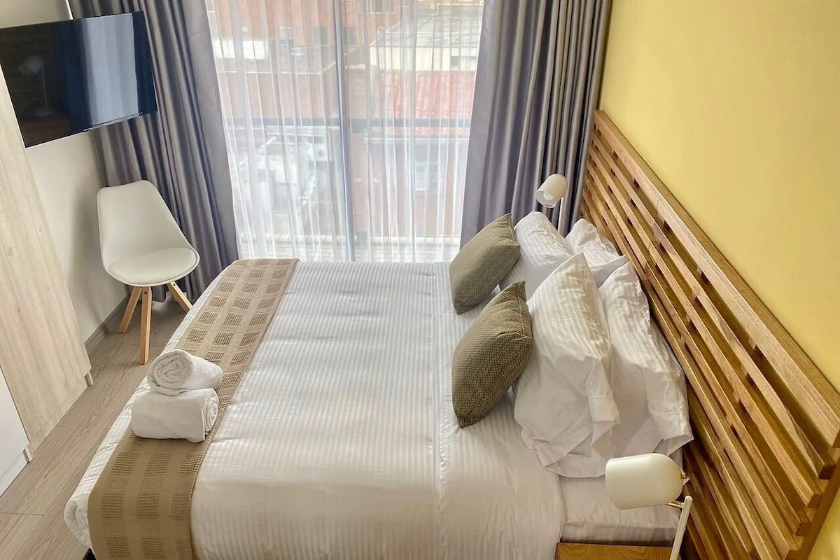 A hotel room with a bed, a TV, a chair, and a window with curtains.
