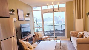 A modern living space with a dining area, kitchen, and seating by a large window. - Modern Whitby 3 Bedroom Condo, close to the 401, Trafalgar Castle and Toronto! (Whitby)