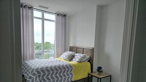 A bedroom with a bed, a nightstand, a window, and a view of greenery outside. - Modern Whitby 3 Bedroom Condo, close to the 401, Trafalgar Castle and Toronto! (Whitby)