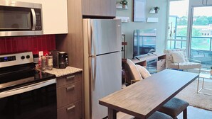 A modern kitchen with stainless steel appliances, a dining area with a wooden table and benches, and a view of the outdoors through large windows. - Modern Whitby 3 Bedroom Condo, close to the 401, Trafalgar Castle and Toronto! (Whitby)