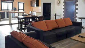 A modern living room with a sectional sofa, a dining area, and a kitchen in the background.