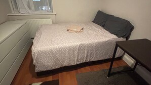 A bedroom with a bed, a bedside table, a window with curtains, and a radiator. - Stylish 1-bed Apartment- Sleeps 3 w/ Central Links (Pinner)