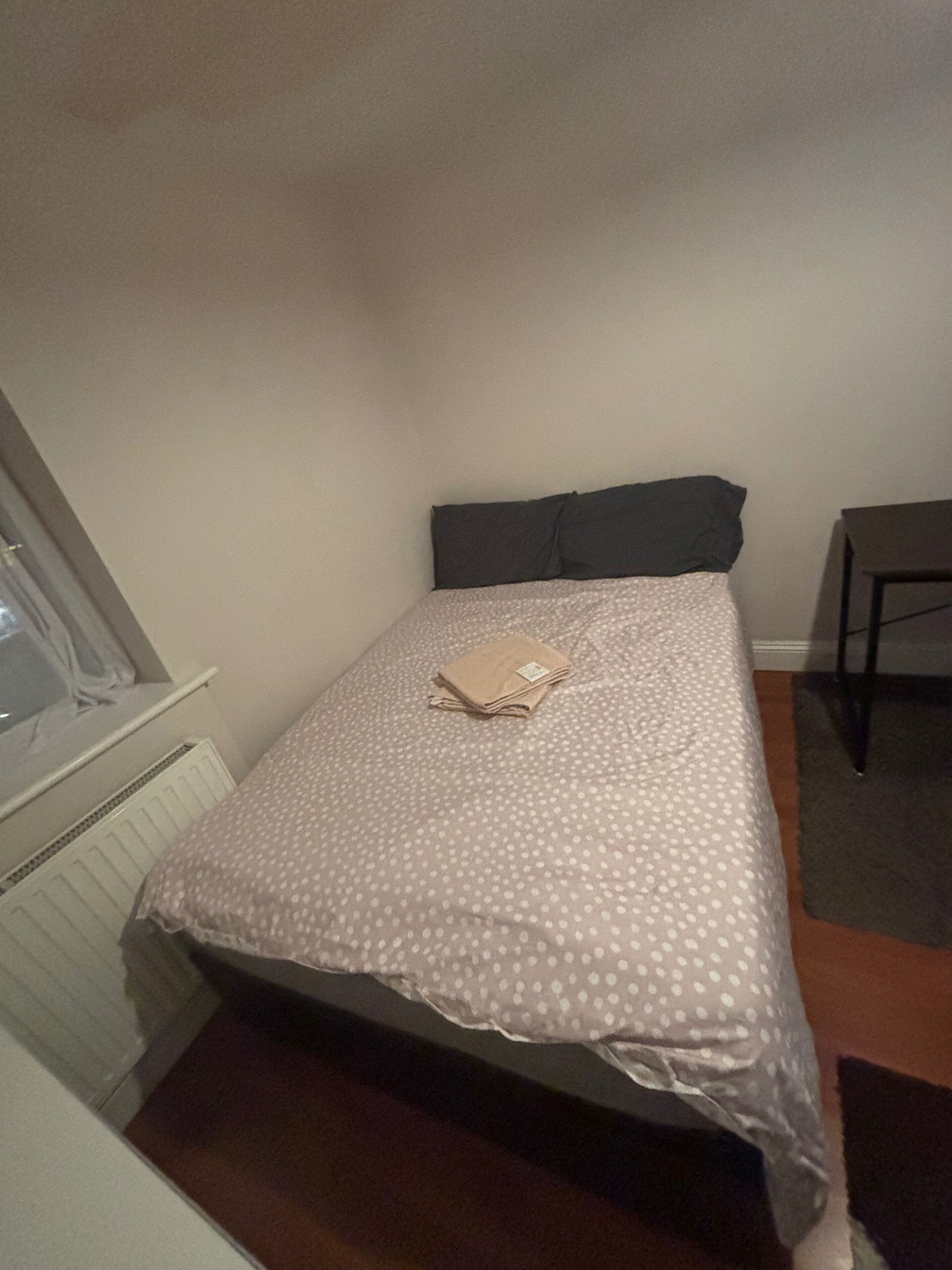 Une petite chambre avec un lit simple, une couvre-lit à pois, une serviette pliée sur le lit et un oreiller de couleur sombre.