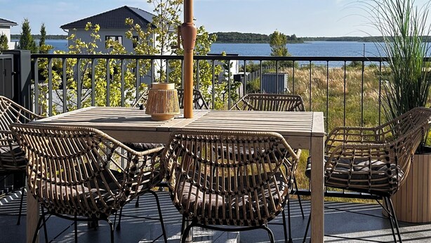 Een terras buiten met een tafel, stoelen en een grote parasol, met uitzicht op het water.