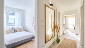 Een moderne slaapkamer met een bed, een grote spiegel en een gang naar een andere kamer.