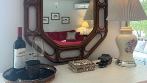 Un espejo con marco de madera, una botella de vino, una copa, una lámpara y objetos decorativos sobre una superficie blanca.