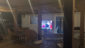 Un patio al aire libre con una mesa y sillas, un televisor y luces colgantes.