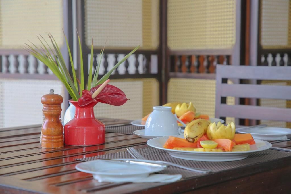 Una mesa dispuesta con platos de fruta, un florero rojo con hojas verdes y una jarra blanca.
