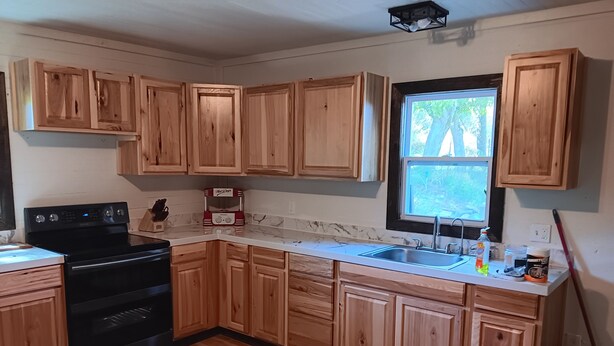 A kitchen with wooden cabinets, a black stove, a window, and a sink.