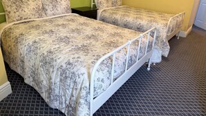 Due letti singoli con biancheria da letto floreale, una struttura in metallo bianco e un pavimento a scacchi.
